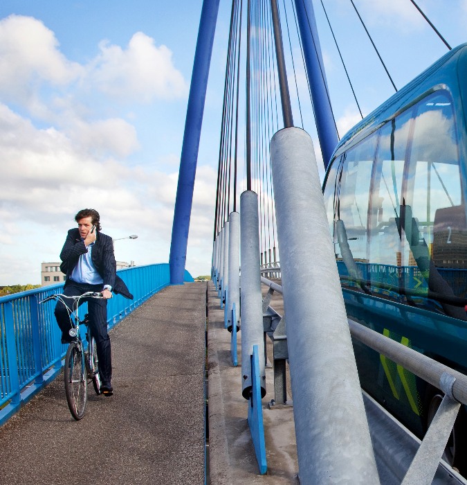 Bridge with cyclist on the left side of the road and on the right the ParkShuttle. This is an electrically-driven, autonomous shuttle service in Rotterdam.